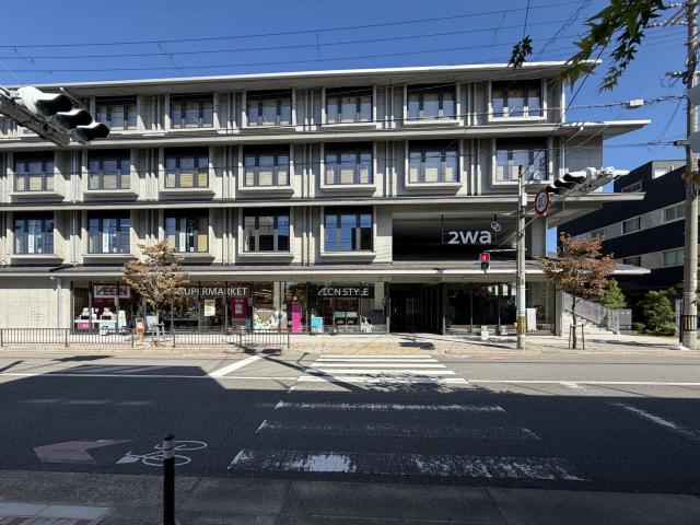 左京区の2waを正面から見た外観。打ち放しコンクリートの4階建てで、1階にスーパーマーケット、右手に「2wa」のサインがある通路と外階段、手前に横断歩道