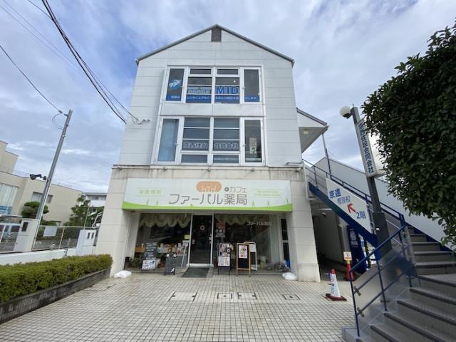 日章ビルの正面外観。白い3階建てで1階に薬局が入り、2階と3階に大きな窓、右手に2階へ上がる外階段