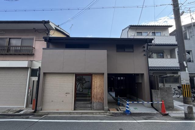 観世町テナントの正面外観。グレージュの外壁の2階建てで、1階にシャッターと木枠のガラス戸、右手に奥へ続く屋根付きの通路がある