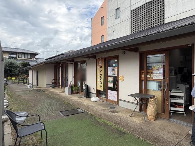 まえだ農園コミュニティーShopの通路側。人工芝と洗い出し舗装の通路に沿って、木枠のガラス引き戸が並ぶ平屋の店舗棟